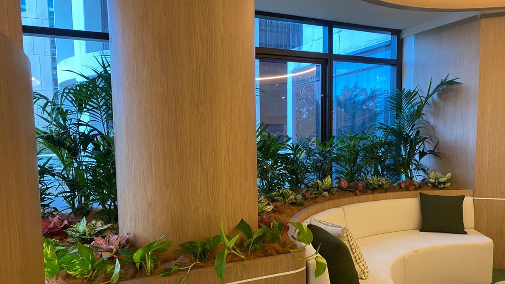 A curved banquette lounge wrapped by a custom planter bed — a Grolife Indoor Plantscapes permanent install featuring palms, dracaena, caladium and trailing pothos