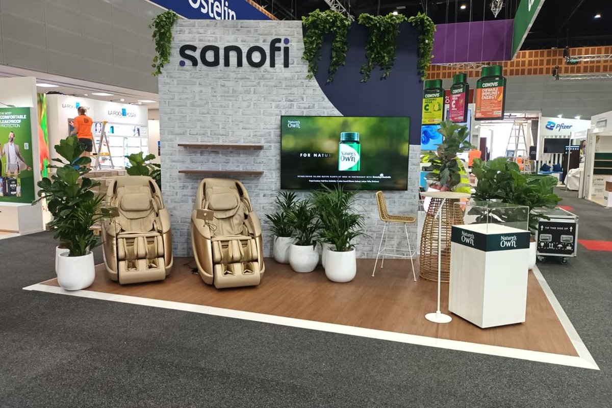 A Sanofi / Nature's Own corporate booth at an expo, styled with kentia palms, fiddle leaf figs and hanging pothos vines by Grolife Indoor Plantscapes