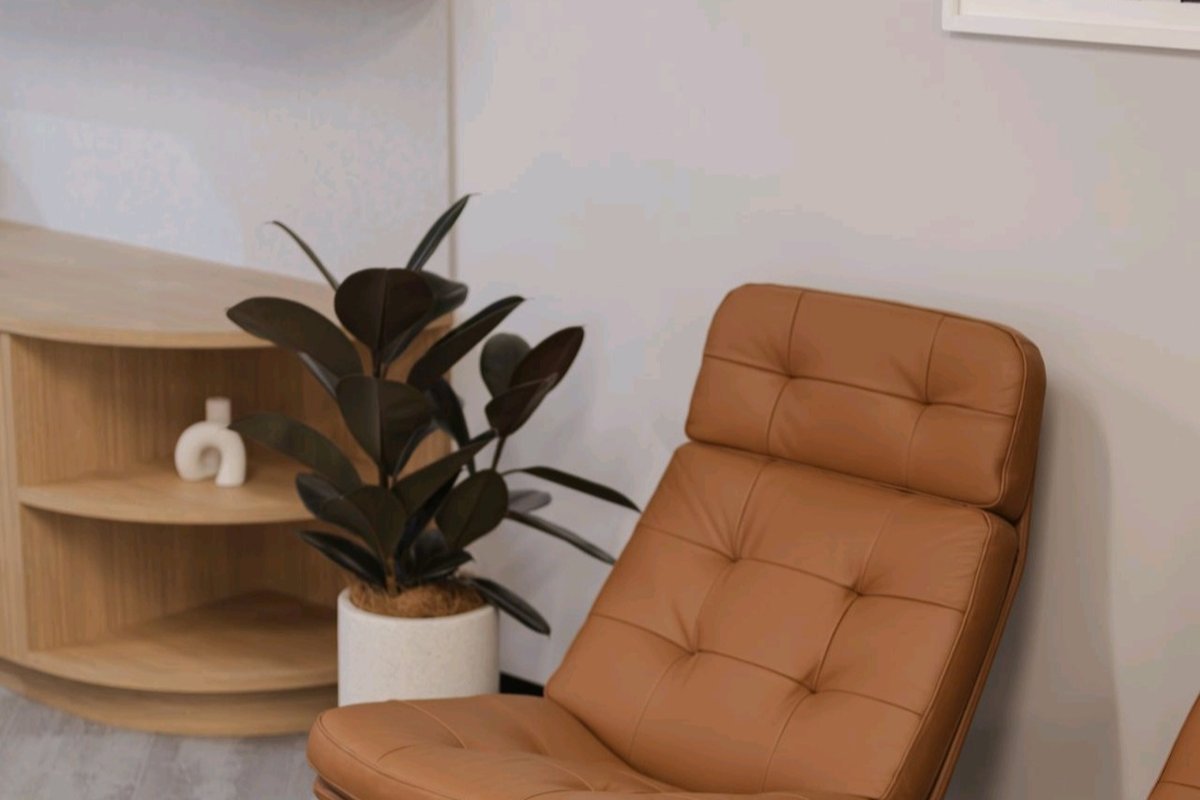 A premium apartment display suite with a tan leather lounge chair, travertine coffee table and a Grolife Indoor Plantscapes burgundy rubber plant