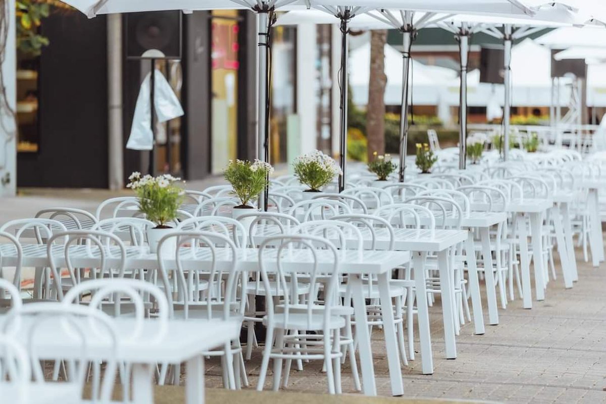 A private outdoor function styled with white bentwood chairs, white tables, market umbrellas and small daisy centrepieces by Grolife Indoor Plantscapes